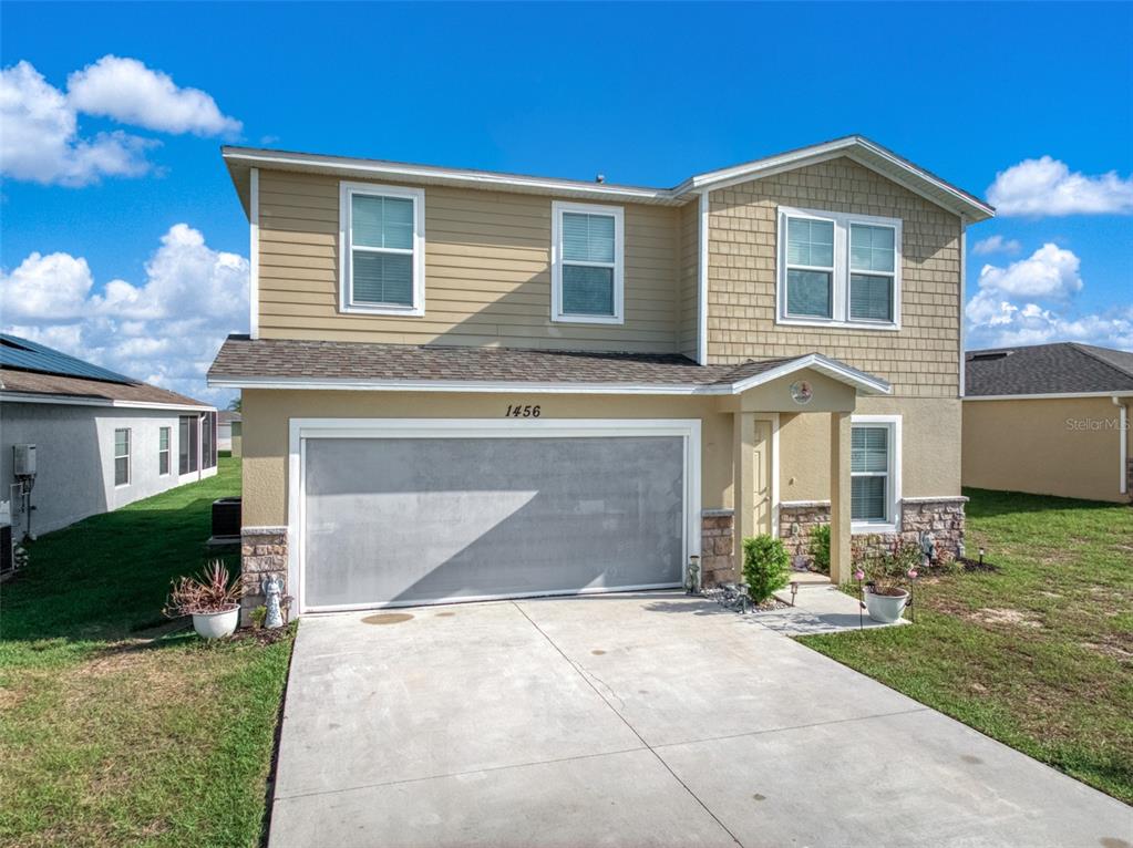 A two-story suburban house with tan siding, a stone facade, and a two-car garage — 1456 STONE RIDGE CIRCLE, SEBRING, FL