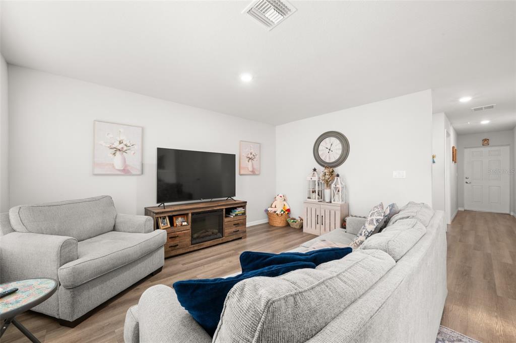 A living room features light gray walls, wood-look flooring, a television console, and gray sofas — 1456 STONE RIDGE CIRCLE, SEBRING, FL