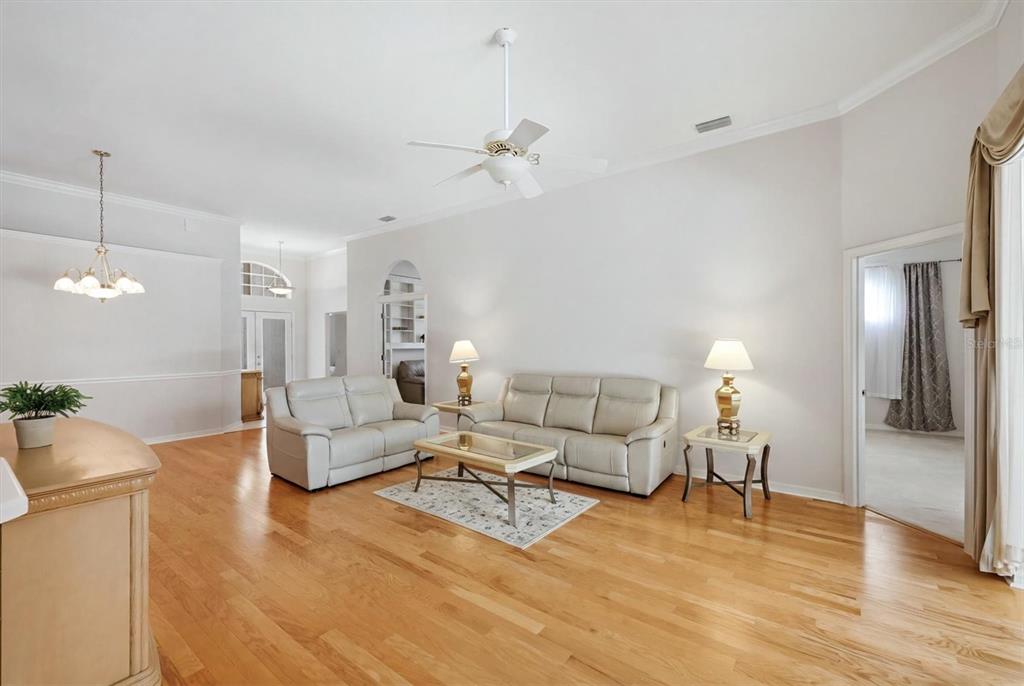 A living room with light-colored leather sofas, hardwood floors, and a ceiling fan — 8492 IDLEWOOD COURT, LAKEWOOD RANCH, FL