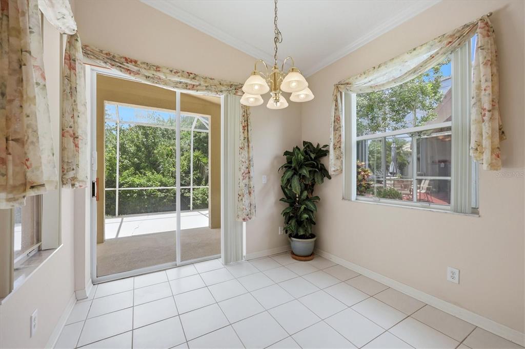 A bright dining area features white tile floors, a chandelier, and a sliding glass door — 8492 IDLEWOOD COURT, LAKEWOOD RANCH, FL