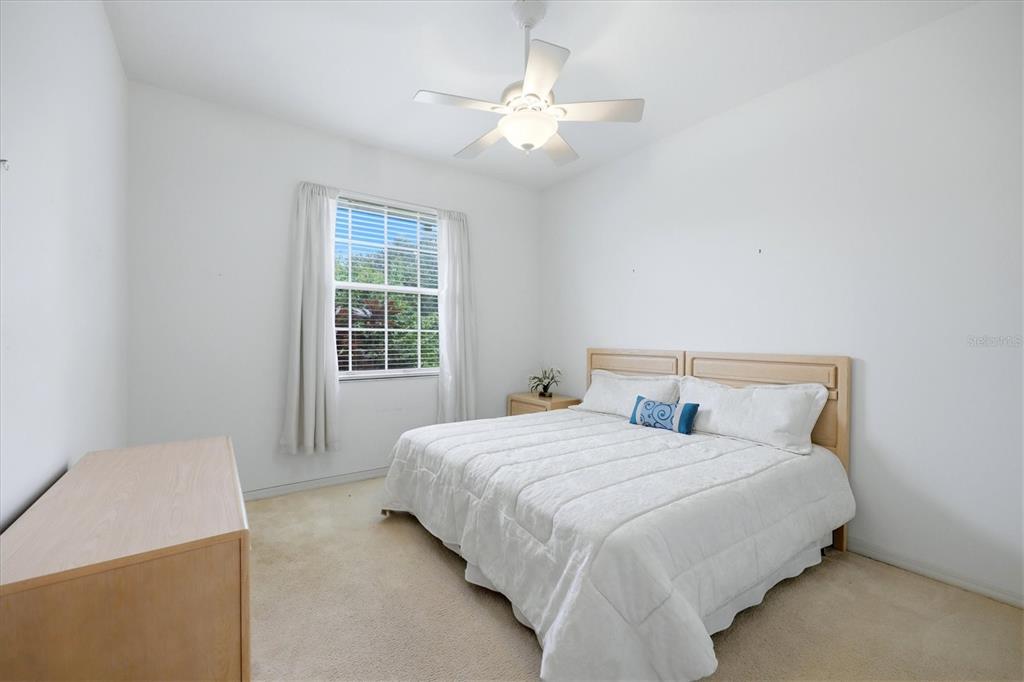 A bedroom features a bed with a white comforter, a ceiling fan, and a window — 8492 IDLEWOOD COURT, LAKEWOOD RANCH, FL