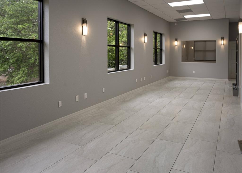 An empty room features gray walls, large windows, wall-mounted light fixtures, and light-colored tile flooring — 1445 E MITCHELL HAMMOCK ROAD UNIT 1, OVIEDO, FL