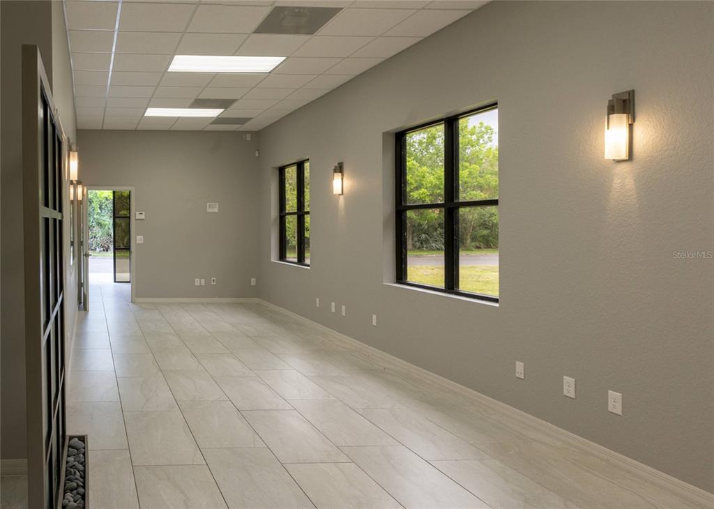 An empty office space features light-colored tile flooring, gray walls, large windows, and recessed lighting — 1445 E MITCHELL HAMMOCK ROAD UNIT 1, OVIEDO, FL