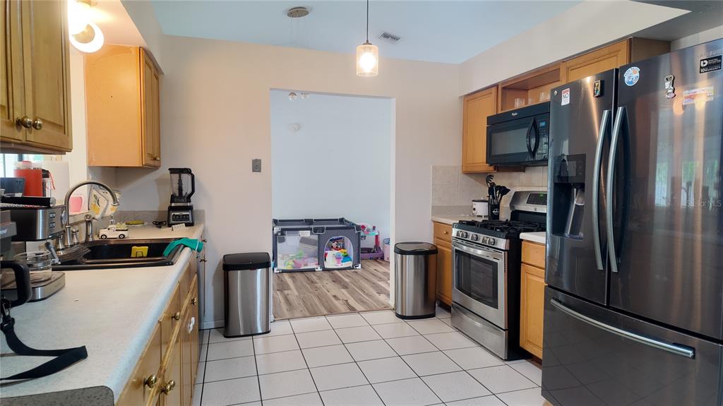A kitchen features wood cabinets, stainless steel appliances, white tile flooring, and a pass-through opening — 304 SHADOW OAK DRIVE, CASSELBERRY, FL