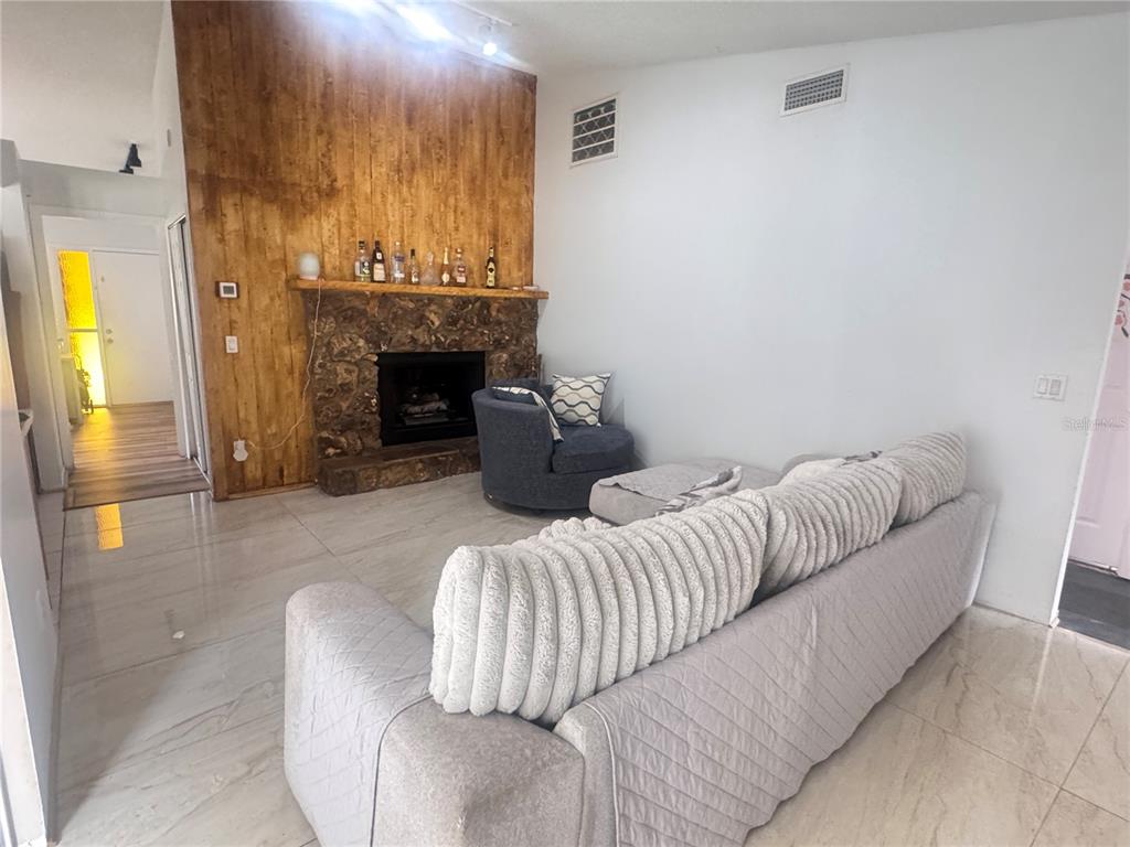 A living room features a stone fireplace, wood-paneled accent wall, light tile flooring, and furniture — 304 SHADOW OAK DRIVE, CASSELBERRY, FL