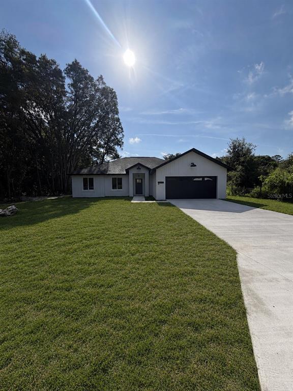 A single-story house with a white exterior, dark garage door, and a large front lawn — 14451 SE 43RD TERRACE, SUMMERFIELD, FL