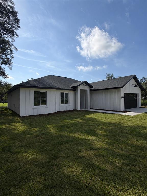 A white board-and-batten single-story house with a dark roof and an attached garage — 14451 SE 43RD TERRACE, SUMMERFIELD, FL
