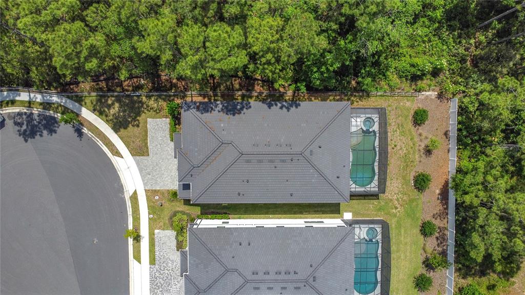 An aerial view shows two houses with dark roofs, screened-in pools, and paved driveways near woods — 1326 BUTTERFLY ORCHID ROAD, DAVENPORT, FL