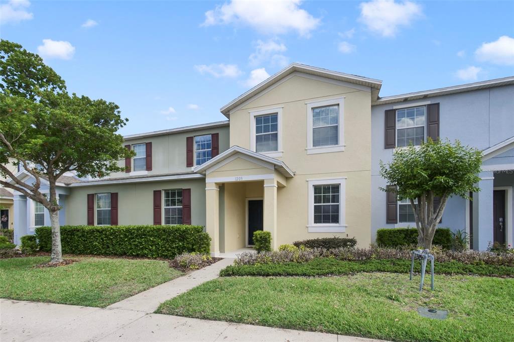 A two-story townhouse with a beige stucco facade, dark shutters, and a covered front entryway — 1209 SEBURN ROAD, APOPKA, FL