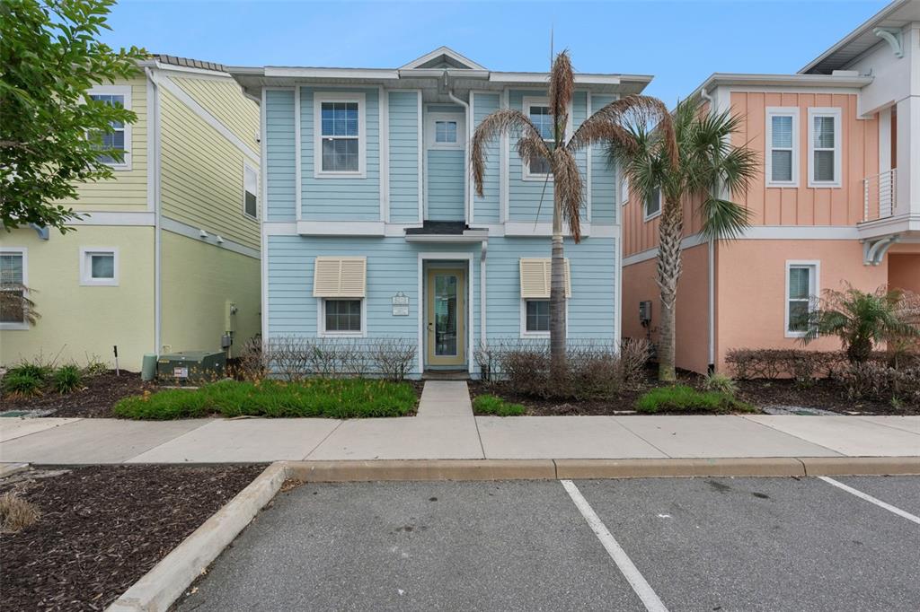 A light blue two-story house with a palm tree stands between yellow and peach homes — 8019 KNEE DEEP ROAD, KISSIMMEE, FL