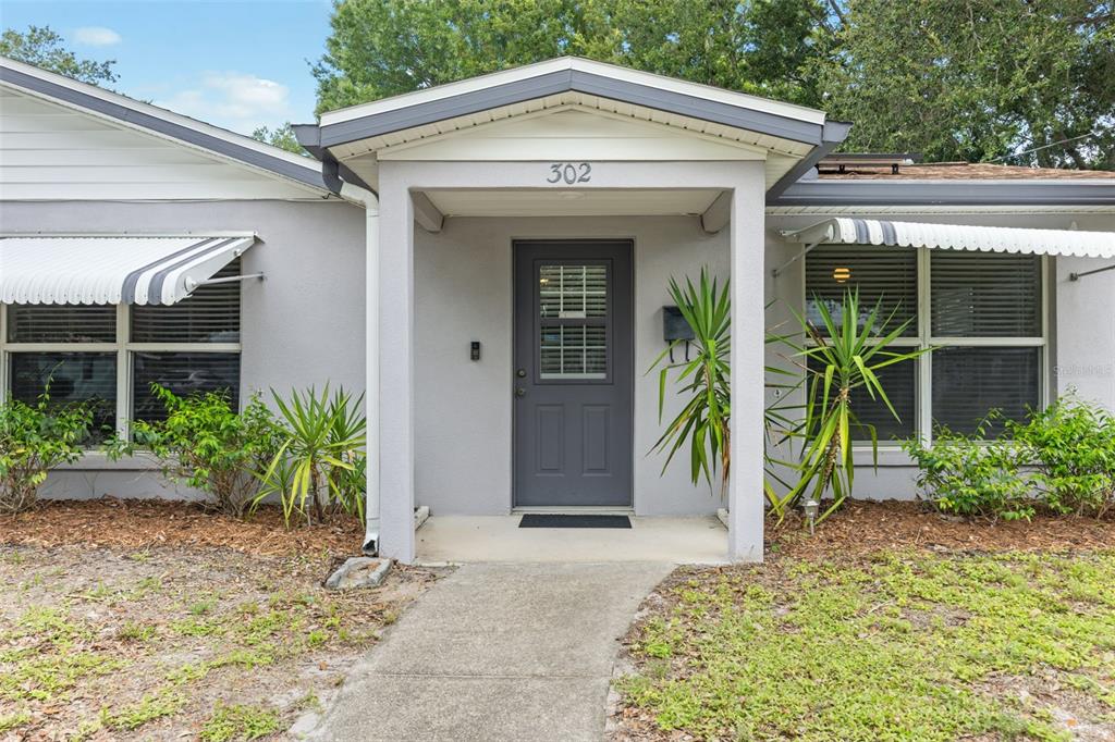 The exterior of a gray house features a covered entryway with a dark gray door — 302 51ST STREET W, BRADENTON, FL