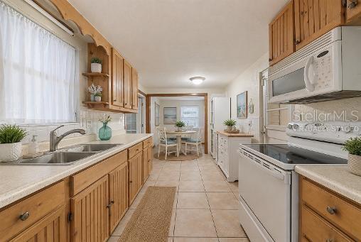 A kitchen with wood cabinets, light countertops, tile flooring, and a view into the dining area — 302 51ST STREET W, BRADENTON, FL