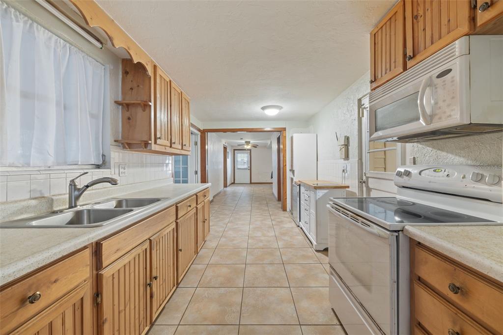 A galley kitchen features wood cabinets, tile flooring, and white appliances — 302 51ST STREET W, BRADENTON, FL