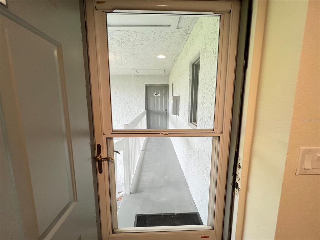 A view through a screen door looking out onto an exterior apartment building walkway — 572 FAIRWAYS LANE UNIT N204, OCALA, FL