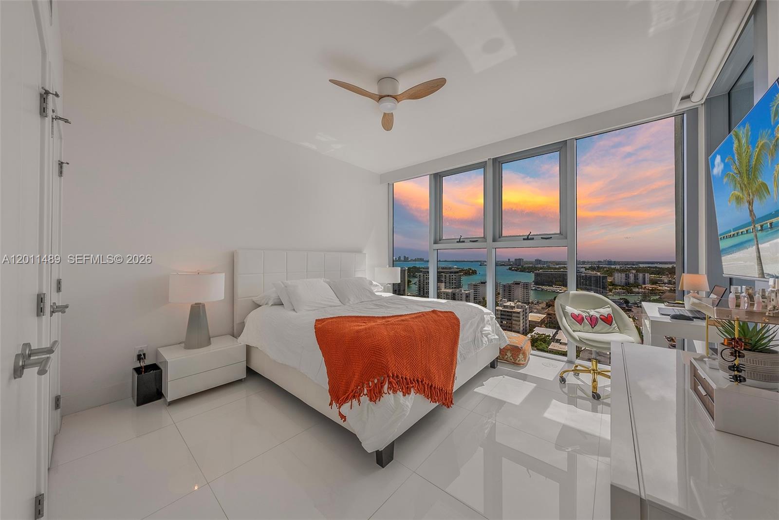 A modern bedroom features a white bed, tiled floors, and floor-to-ceiling windows overlooking a city — 6899 Collins Ave # 2004, Miami Beach FL 33141, MIAMI BEACH, FL