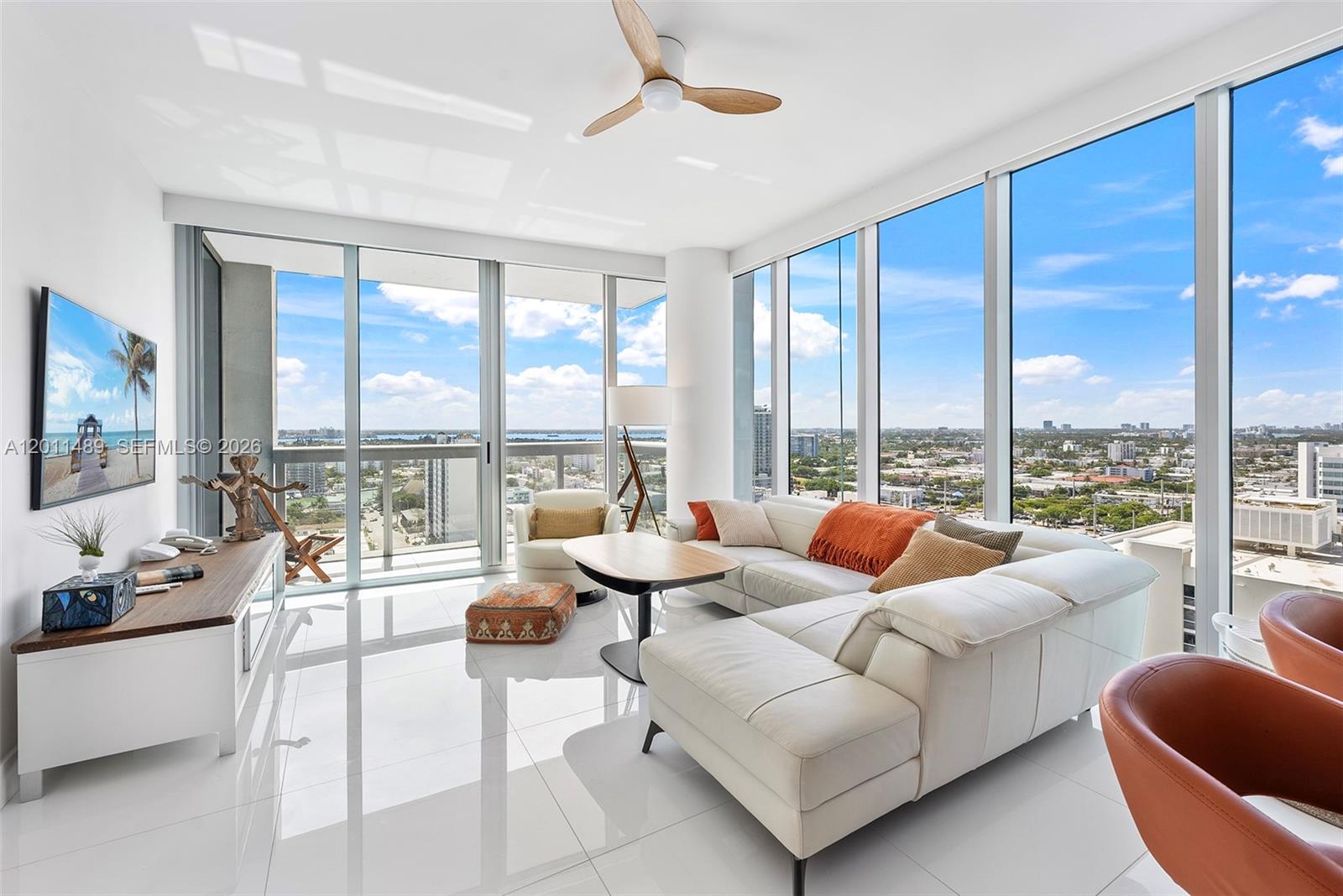 A modern living room features white tile floors, a sectional sofa, and floor-to-ceiling windows — 6899 Collins Ave # 2004, Miami Beach FL 33141, MIAMI BEACH, FL