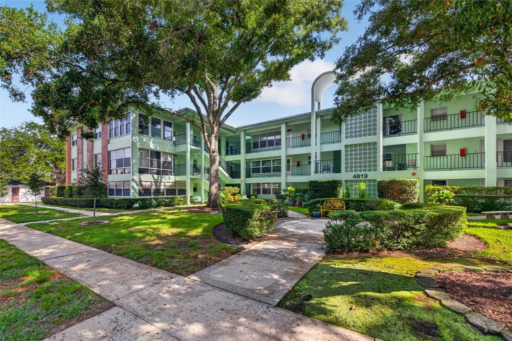 A three-story apartment building with light green exterior walls and balconies surrounded by landscaping — 4819 8TH AVENUE N UNIT 201, ST PETERSBURG, FL