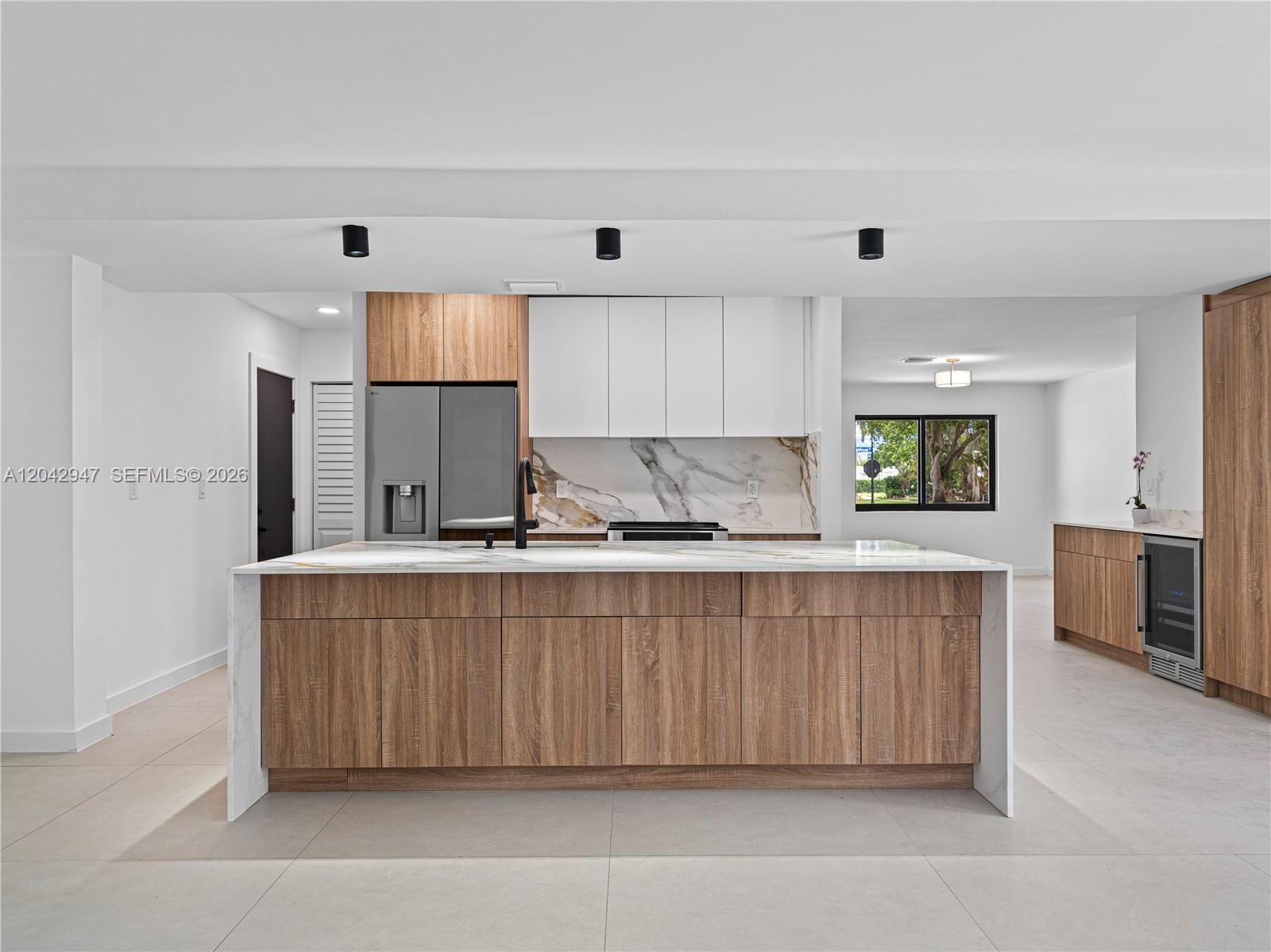 A modern kitchen features a large marble-topped island, wood cabinetry, and white upper cabinets — 949 Lighthouse Dr, North Palm Beach FL 33408, NORTH PALM BEACH, FL
