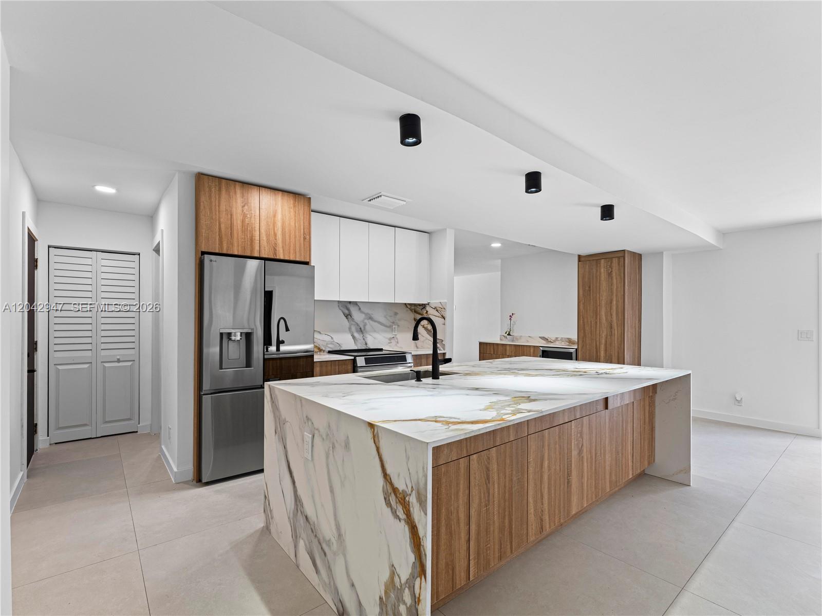 A modern kitchen features a large marble waterfall island, wood cabinetry, and stainless steel appliances — 949 Lighthouse Dr, North Palm Beach FL 33408, NORTH PALM BEACH, FL