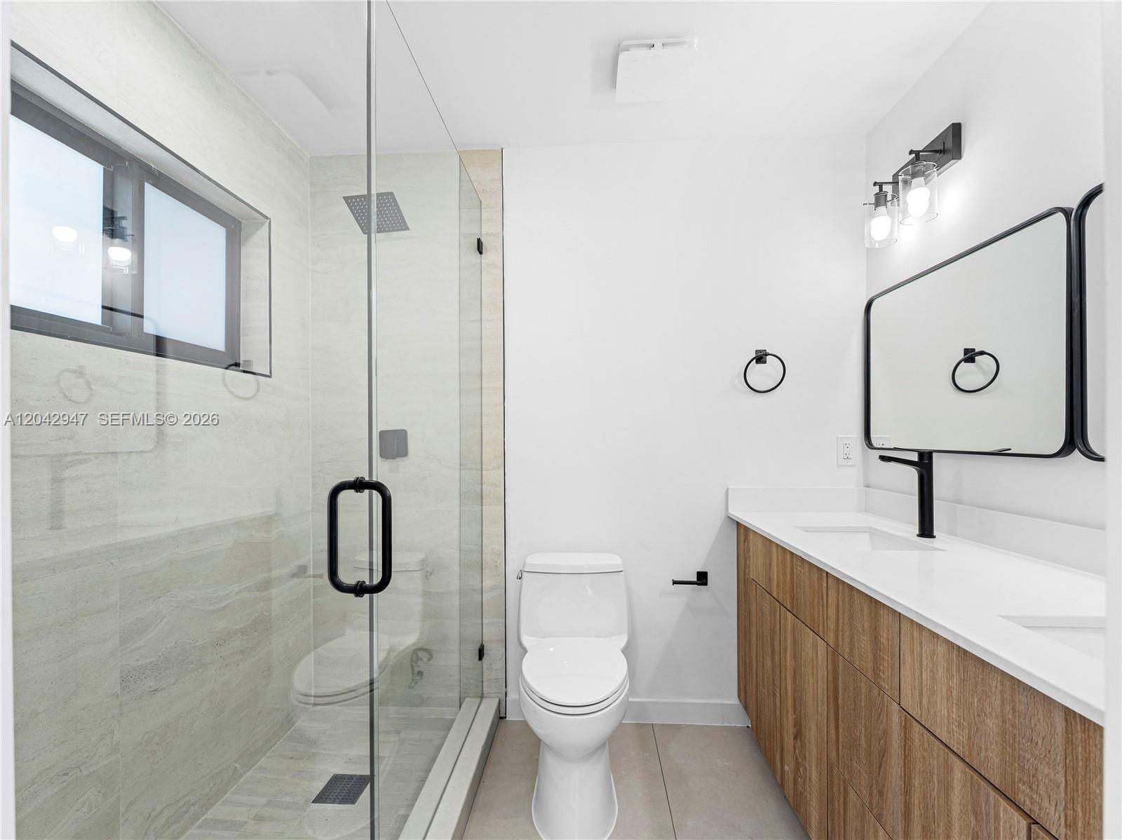 A modern bathroom features a glass-enclosed shower, a white toilet, and a wood-toned vanity — 949 Lighthouse Dr, North Palm Beach FL 33408, NORTH PALM BEACH, FL
