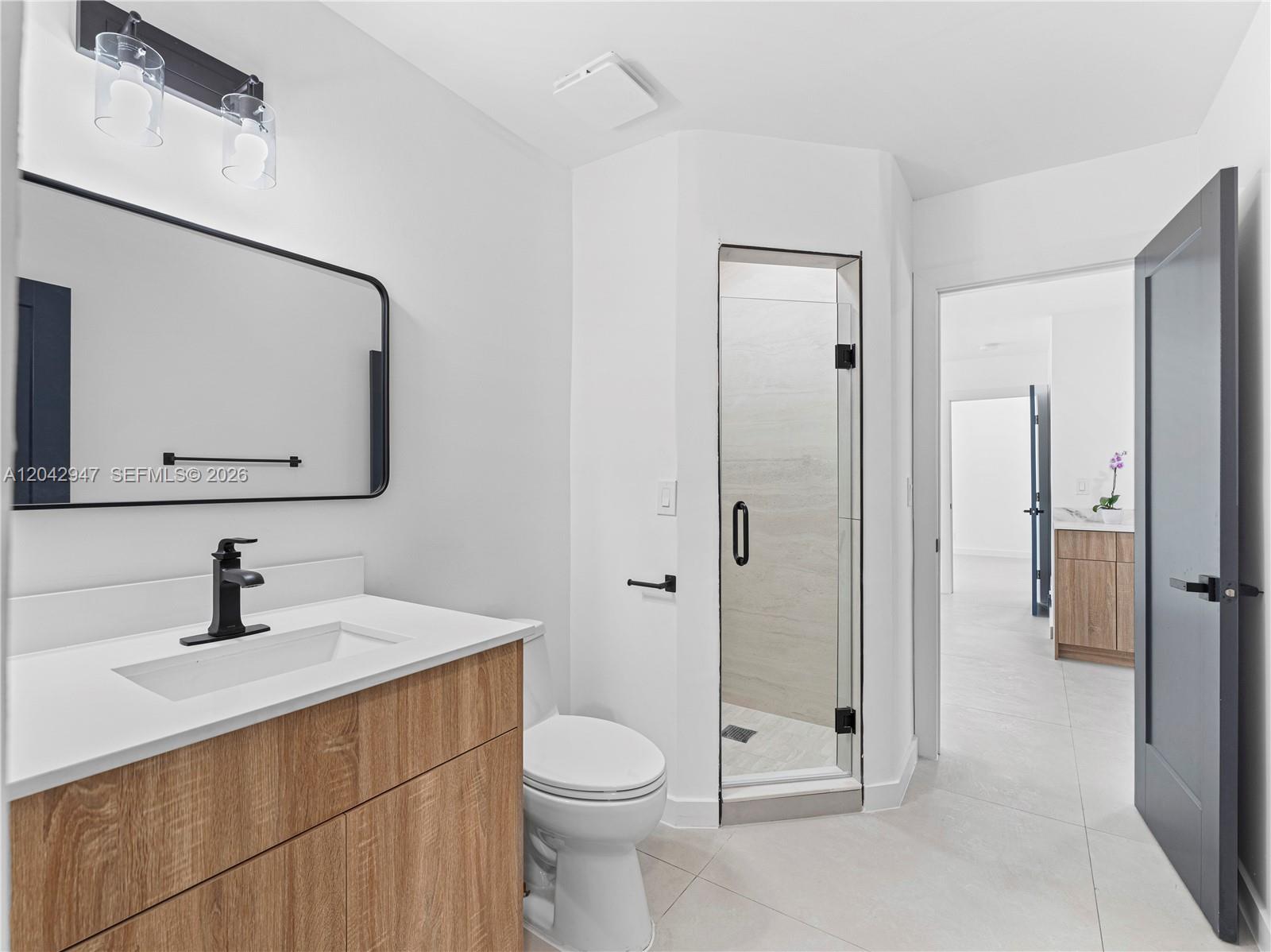A modern bathroom features a wood vanity, black fixtures, a glass shower, and tile flooring — 949 Lighthouse Dr, North Palm Beach FL 33408, NORTH PALM BEACH, FL