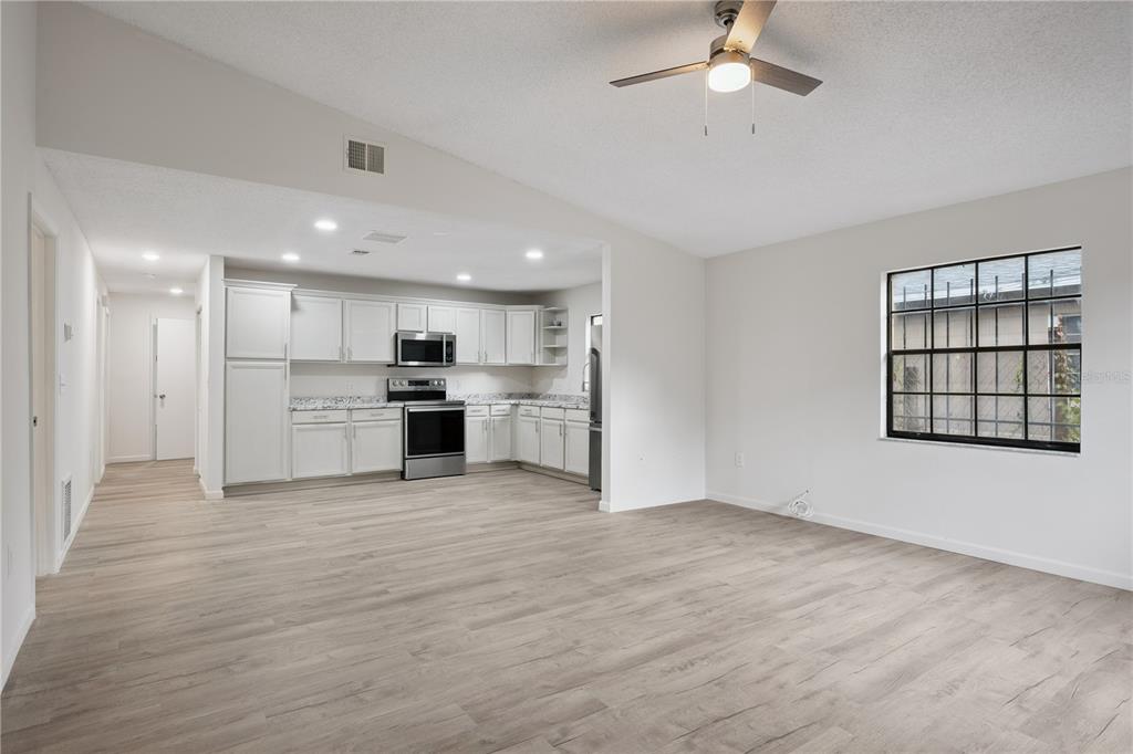 An open-concept kitchen and living area with light wood-look flooring and white cabinetry — 716 GROVE AVENUE, ORLANDO, FL