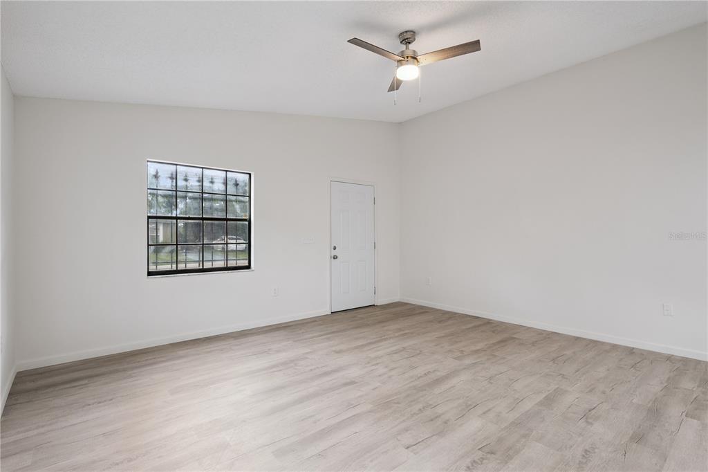 An empty room features light-colored wood-look flooring, white walls, a ceiling fan, and a window with security bars — 716 GROVE AVENUE, ORLANDO, FL
