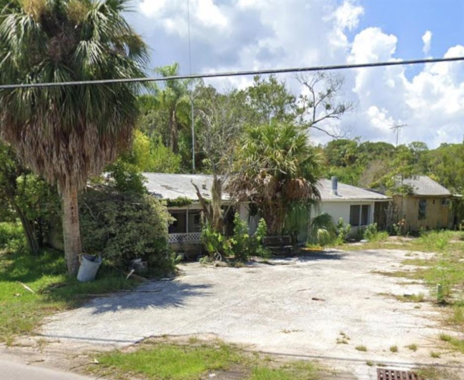 A weathered, single-story house with a large paved driveway and overgrown landscaping — 18909 ARIPEKA ROAD, HUDSON, FL