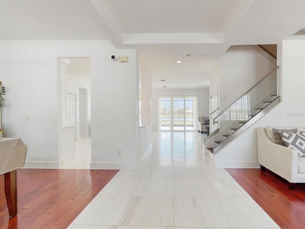 A bright entryway features white tile flooring, a staircase with glass railings, and hardwood accents — 6609 LAKE PEMBROKE PLACE, ORLANDO, FL