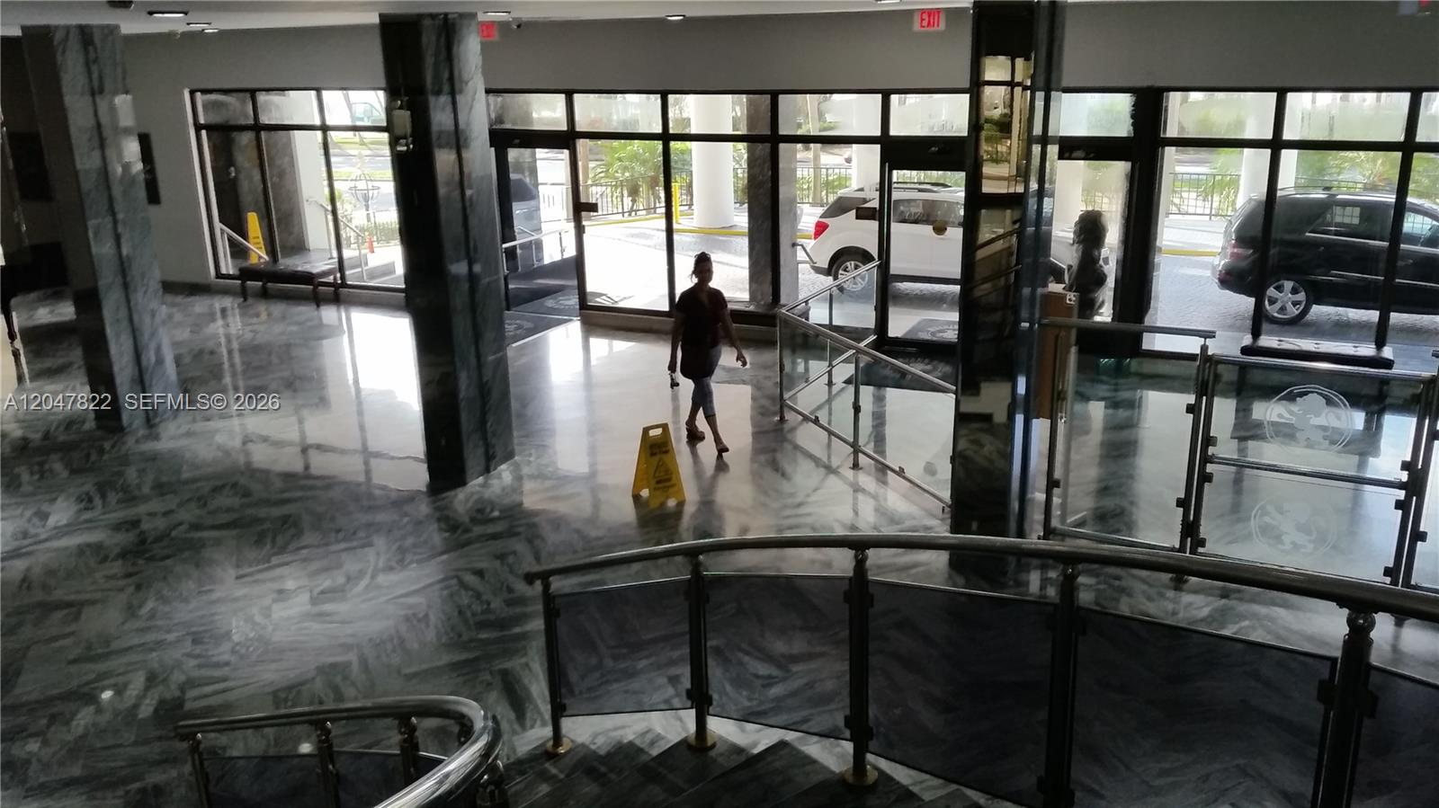 A person walks through a marble-floored lobby with glass railings and large exterior windows — 5401 Collins Ave # 311, Miami Beach FL 33140, MIAMI BEACH, FL