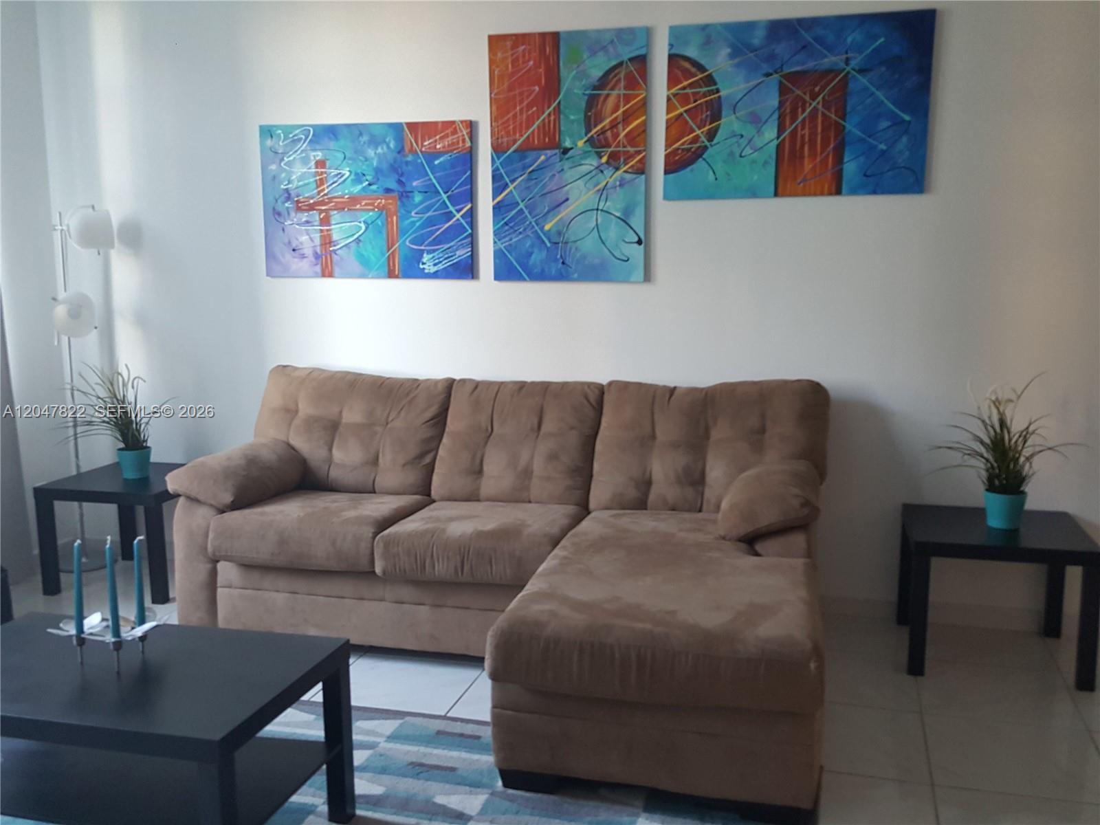 A living room features a brown sectional sofa, a coffee table, and three abstract paintings — 5401 Collins Ave # 311, Miami Beach FL 33140, MIAMI BEACH, FL