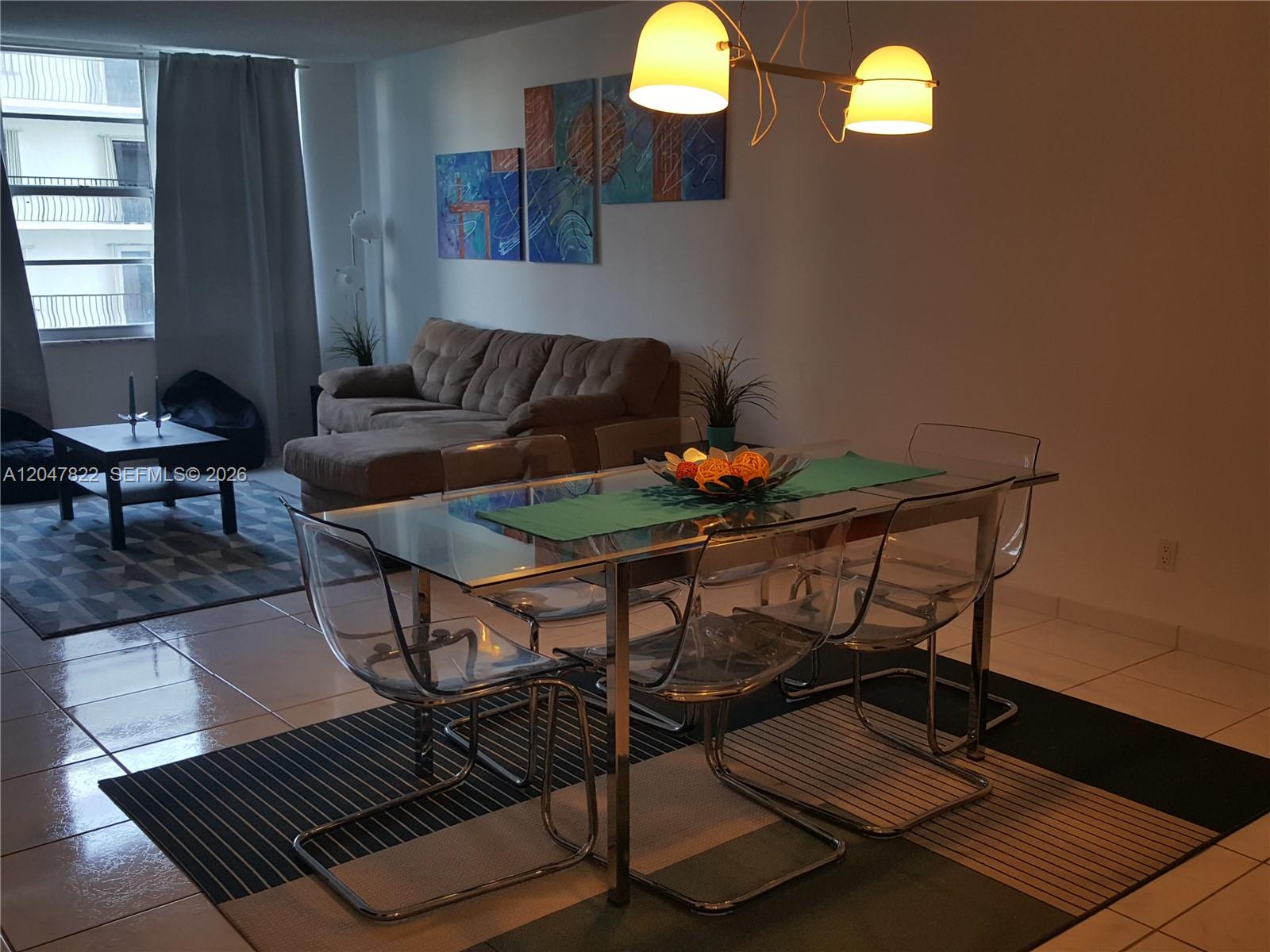 A dining area with a glass table and clear chairs sits before a living room — 5401 Collins Ave # 311, Miami Beach FL 33140, MIAMI BEACH, FL