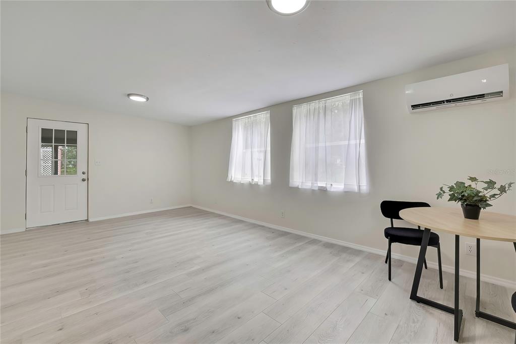 A bright room features light wood-look flooring, two windows with white curtains, and a wall-mounted AC — 5175 E LIVE OAK LANE, INVERNESS, FL