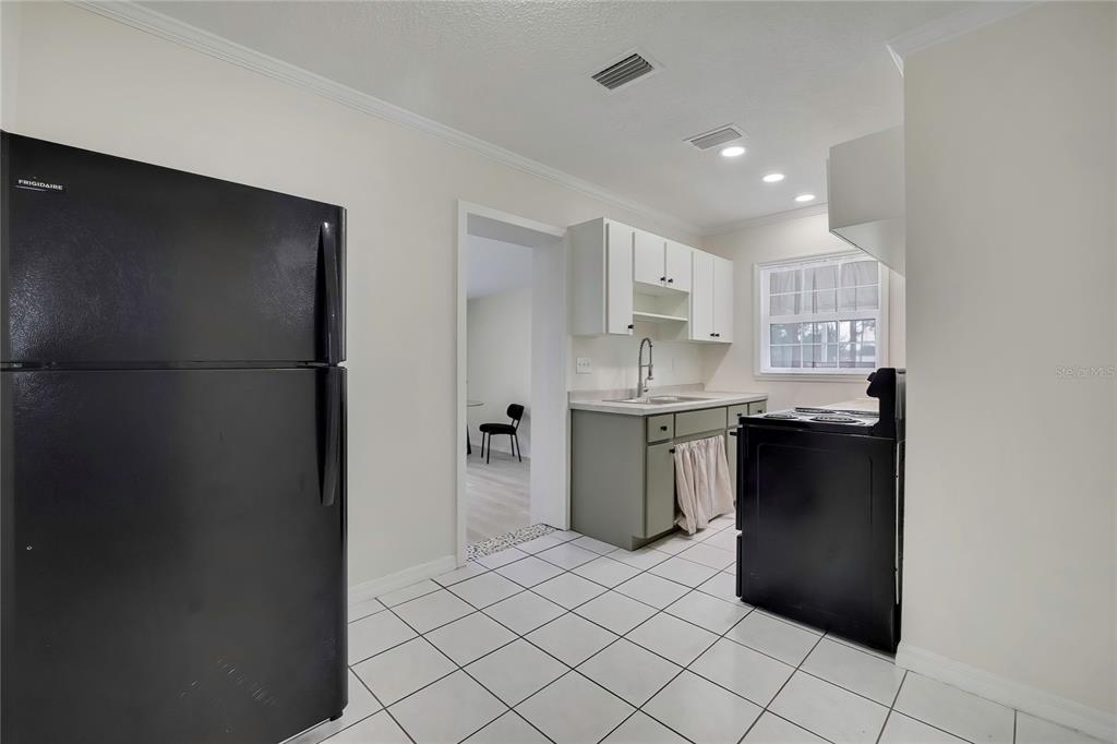 A kitchen features white upper cabinets, sage green lower cabinets, black appliances, and white tile flooring — 5175 E LIVE OAK LANE, INVERNESS, FL