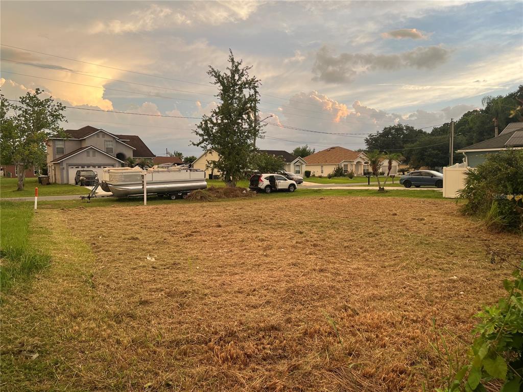 A vacant, grassy residential lot sits in front of suburban houses and a parked pontoon boat — 808 HALIFAX DRIVE, KISSIMMEE, FL