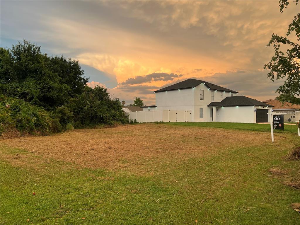 A vacant grassy lot sits in front of a white two-story house at sunset — 808 HALIFAX DRIVE, KISSIMMEE, FL