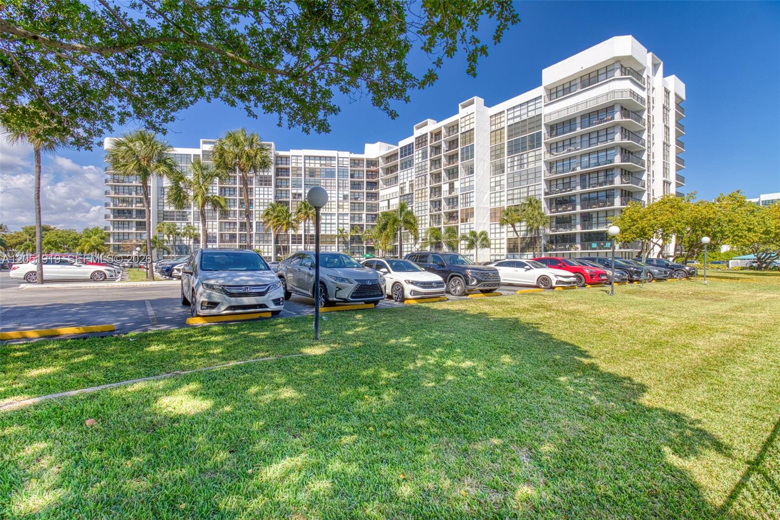 A multi-story white apartment building stands behind a parking lot with several parked cars — 800 Parkview Dr # 311, Hallandale Beach FL 33009, HALLANDALE BEACH, FL