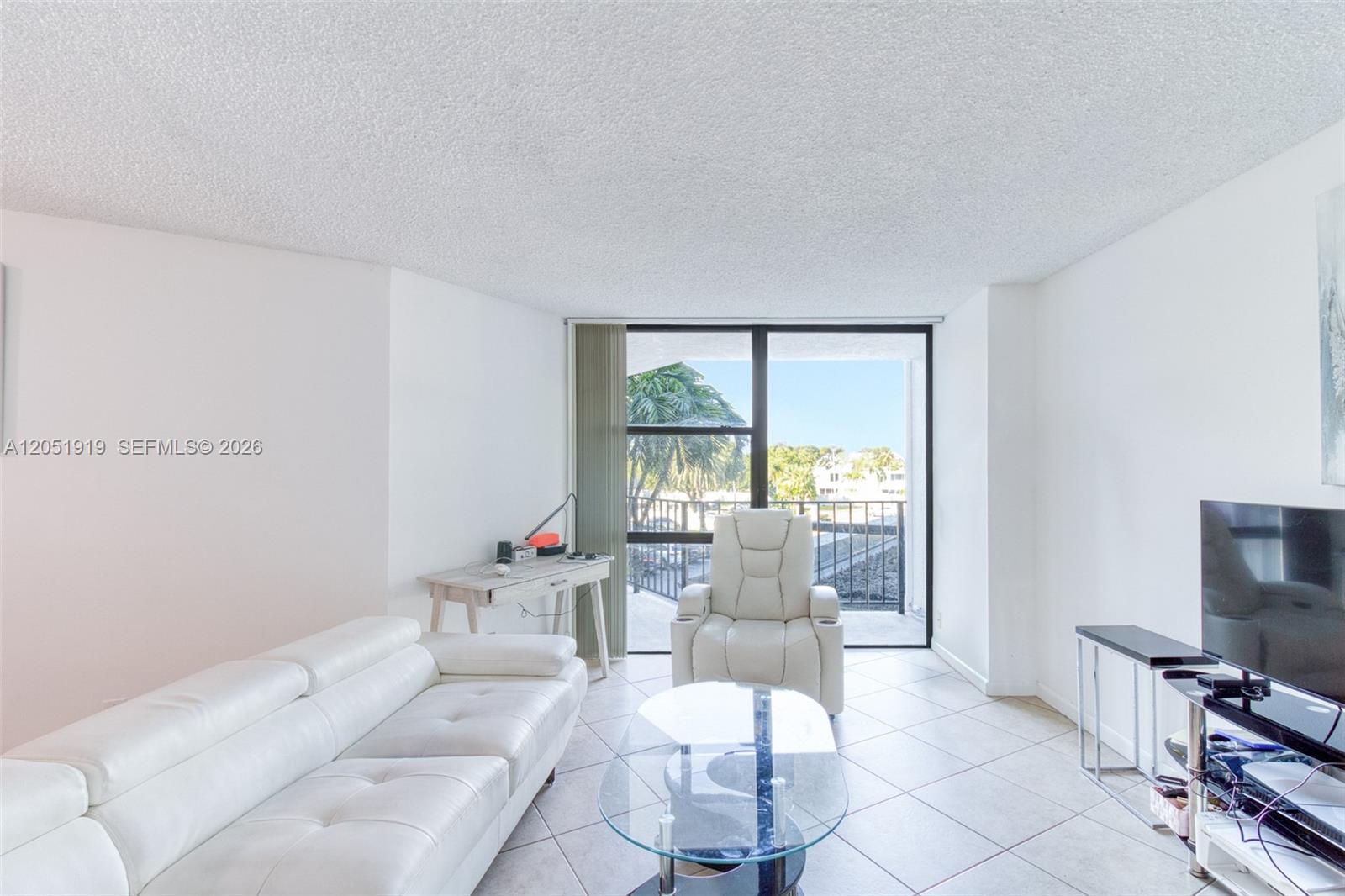 A living room features white leather furniture, a glass coffee table, and a balcony view — 800 Parkview Dr # 311, Hallandale Beach FL 33009, HALLANDALE BEACH, FL