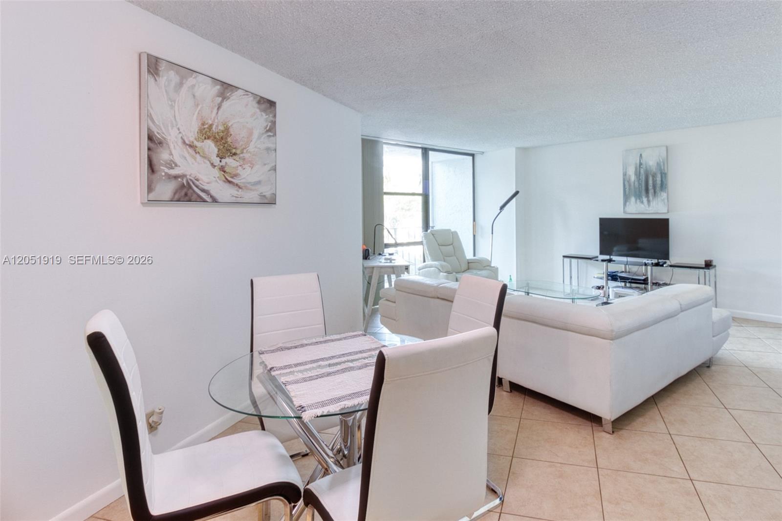 A dining area with a glass table and white chairs opens into a living room — 800 Parkview Dr # 311, Hallandale Beach FL 33009, HALLANDALE BEACH, FL