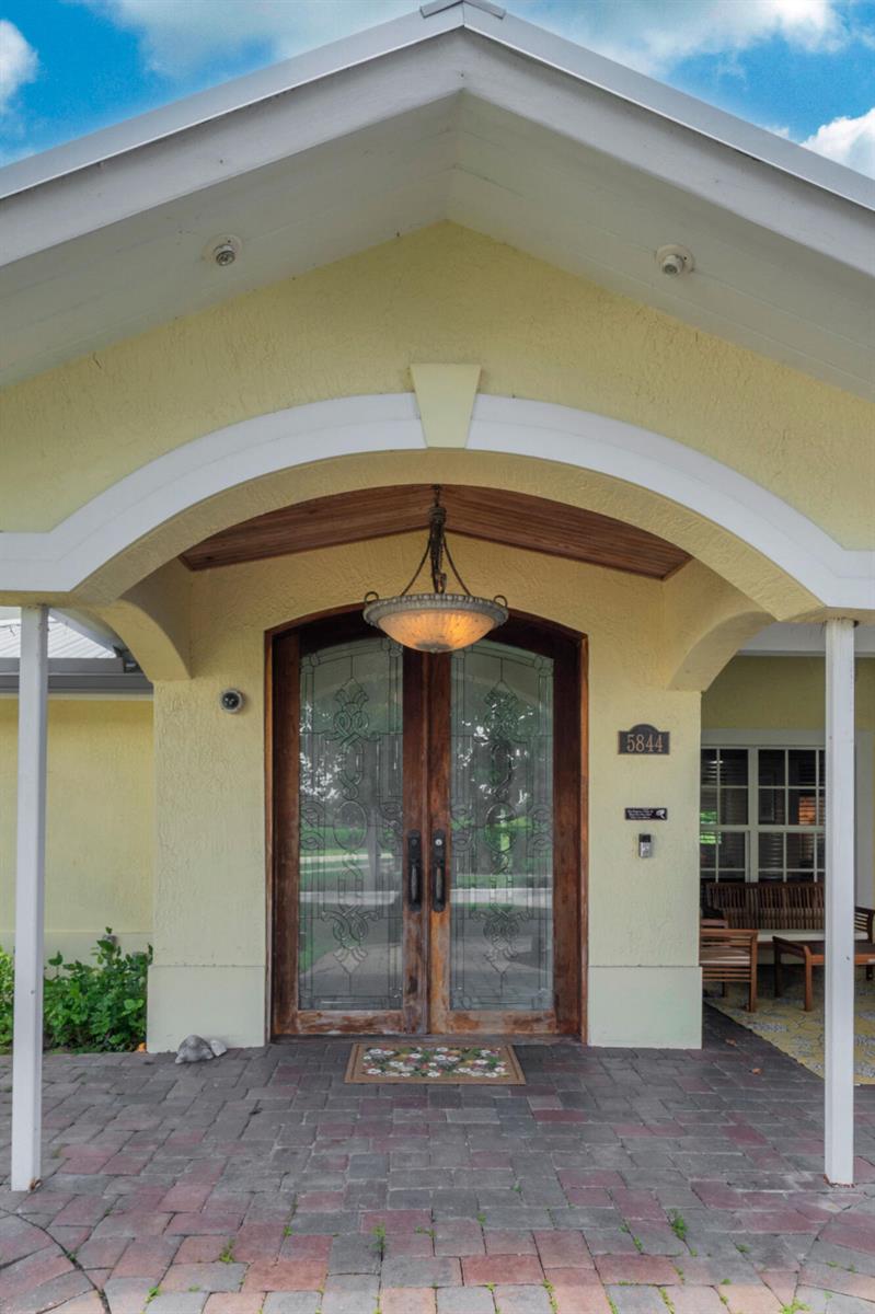A covered entryway with a brick patio, double glass doors, and a decorative hanging light fixture — 5844 Pinebrook Drive, Boca Raton FL 33433, BOCA RATON, FL