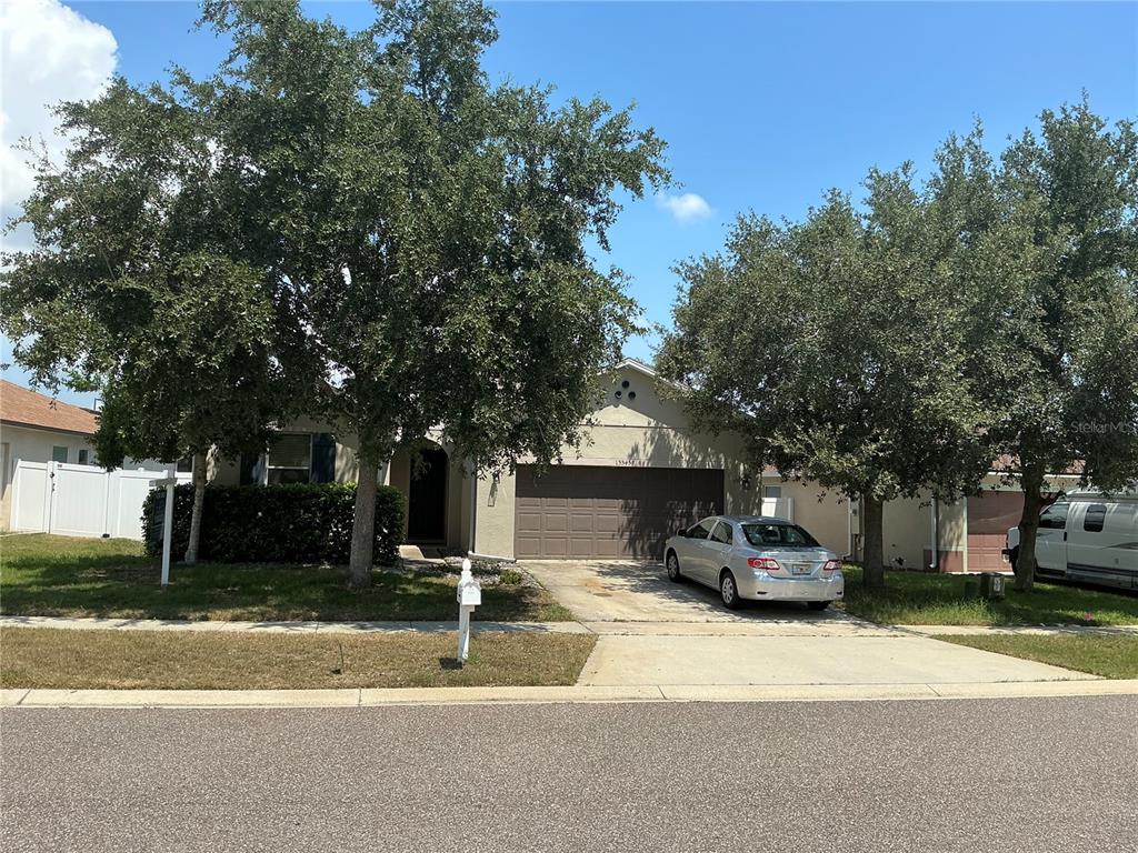 A single-story house with a two-car garage, a concrete driveway, and two large shade trees — 13545 LARANJA STREET, CLERMONT, FL