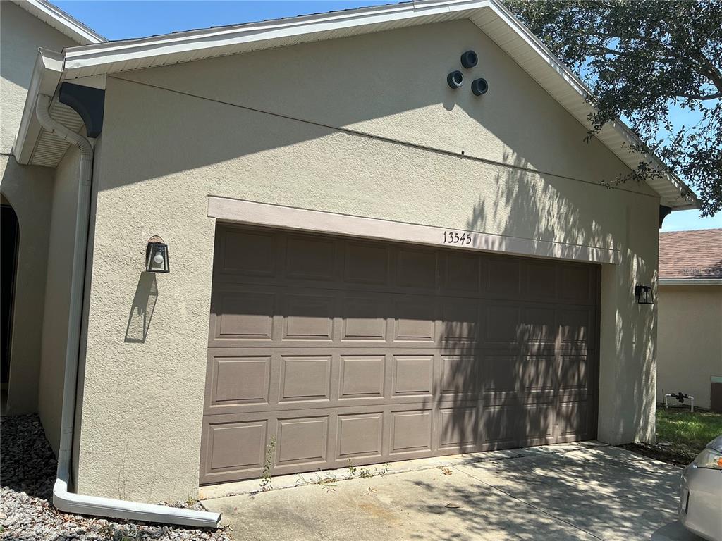 A beige stucco house exterior features a two-car garage with a brown paneled door — 13545 LARANJA STREET, CLERMONT, FL