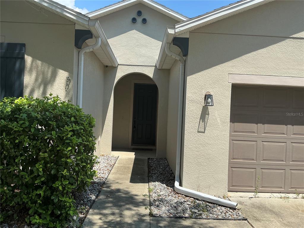 The exterior of a house features a tan stucco facade, a dark door, and garage — 13545 LARANJA STREET, CLERMONT, FL