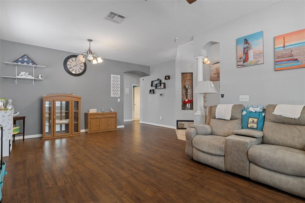 A living room features gray walls, wood-look flooring, a beige sofa, and wall decor — 8483 PINETOP RIDGE LANE, BROOKSVILLE, FL