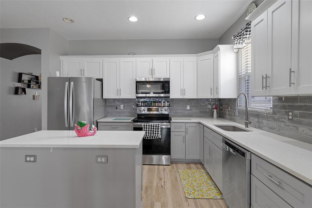 A kitchen features white upper cabinets, gray lower cabinets, stainless steel appliances, and a central island — 8483 PINETOP RIDGE LANE, BROOKSVILLE, FL