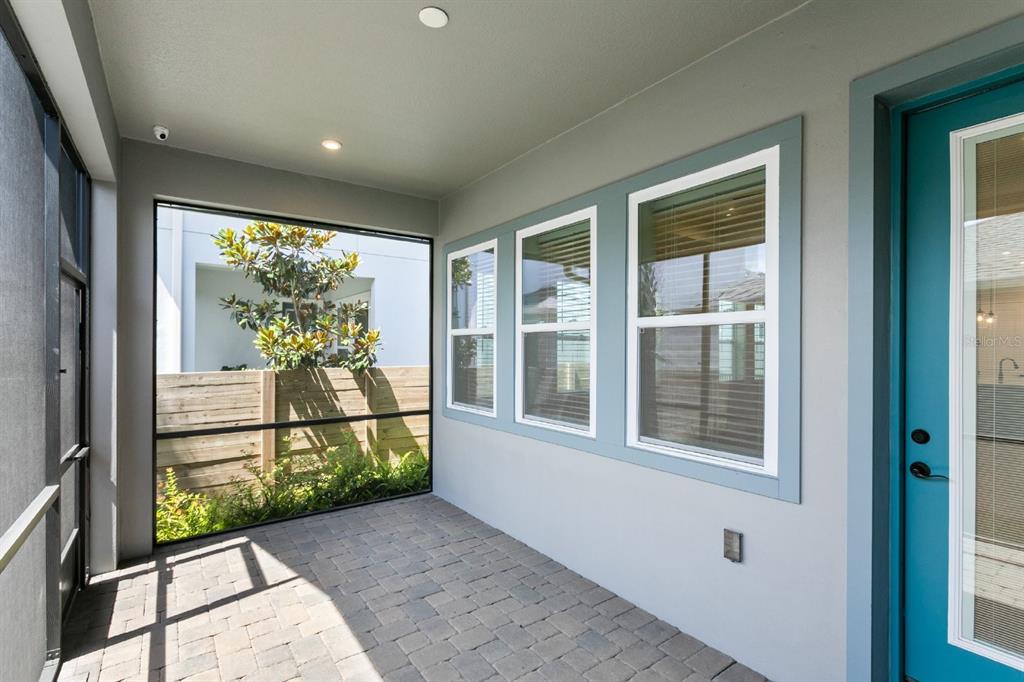 A covered patio features gray walls, a paver floor, three windows, and a teal door — 8828 SPERRY STREET, ORLANDO, FL