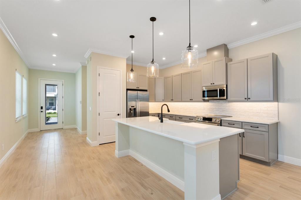 A modern kitchen features light gray cabinets, a white quartz island, and light wood flooring — 8828 SPERRY STREET, ORLANDO, FL