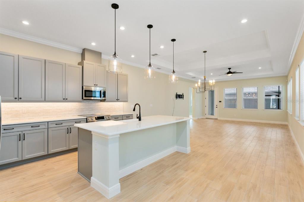 A kitchen with gray cabinets, a white island, and light wood floors in an open room — 8828 SPERRY STREET, ORLANDO, FL
