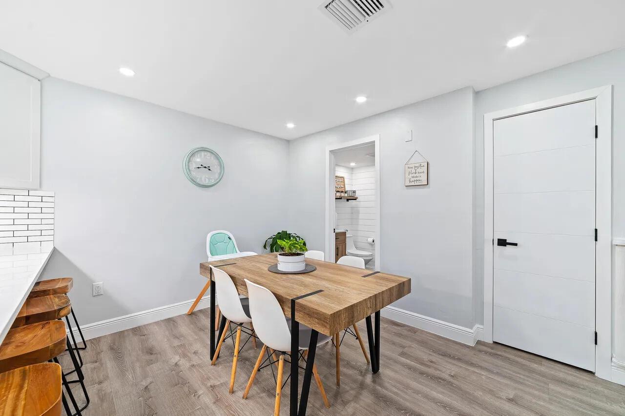A dining area features a wooden table with white chairs, light flooring, and a bathroom doorway — 3132 SW 20th Terrace # 12b, Delray Beach FL 33445, DELRAY BEACH, FL