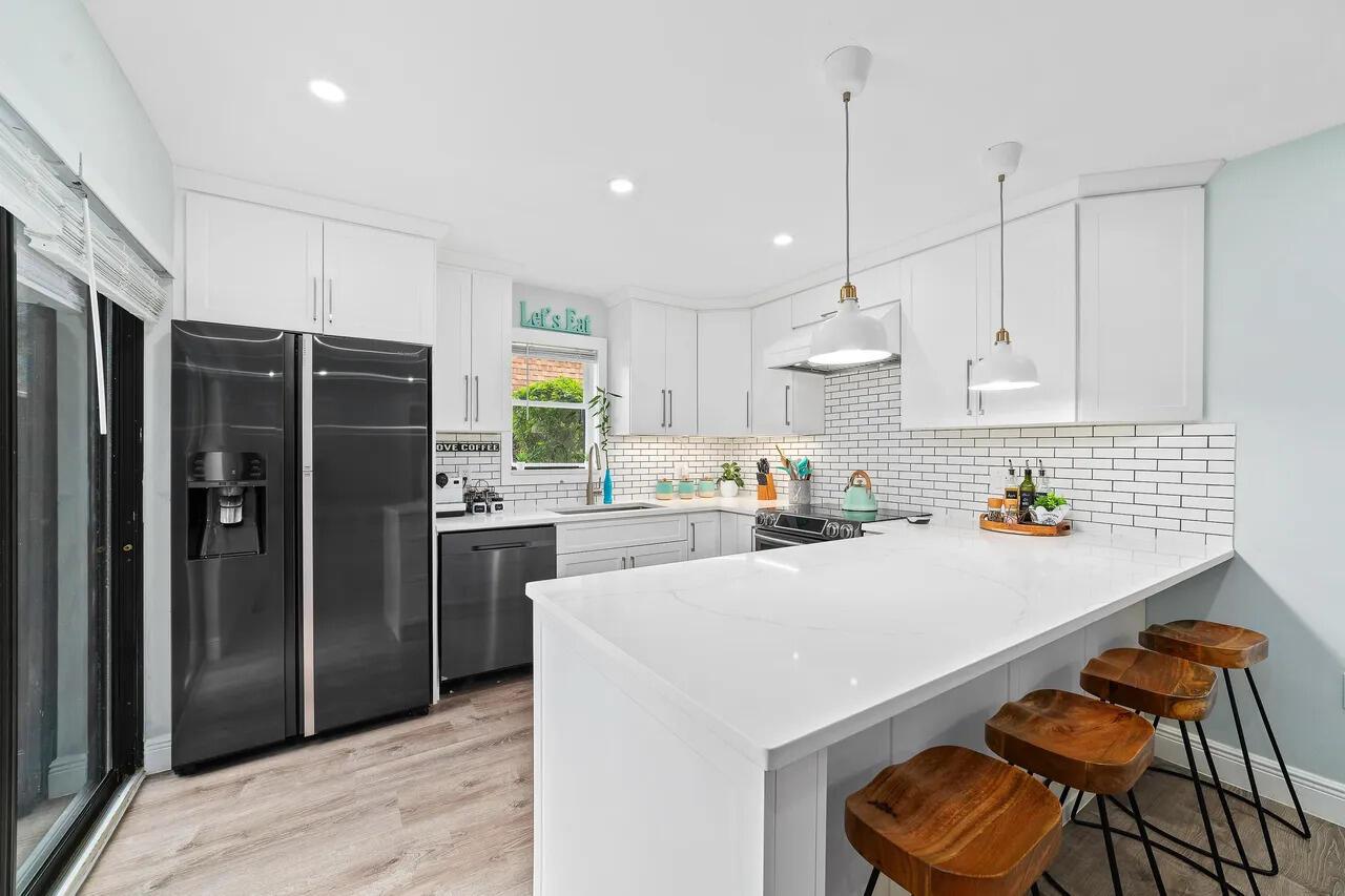 A modern white kitchen features a quartz-topped island with three wooden bar stools — 3132 SW 20th Terrace # 12b, Delray Beach FL 33445, DELRAY BEACH, FL